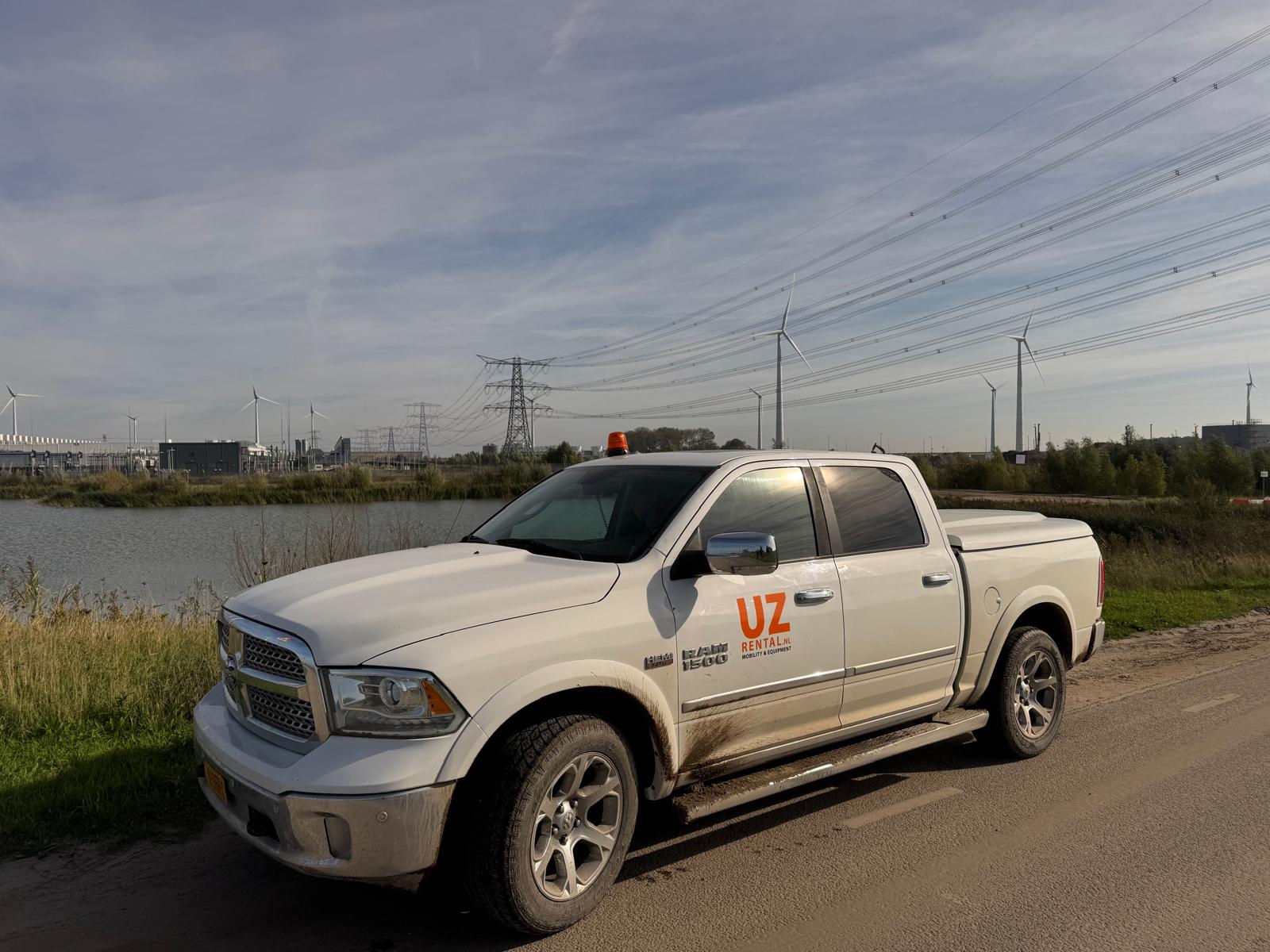 Witte RAM 1500 pick-up van UZ Rental op een projectlocatie met windturbines en hoogspanningslijnen